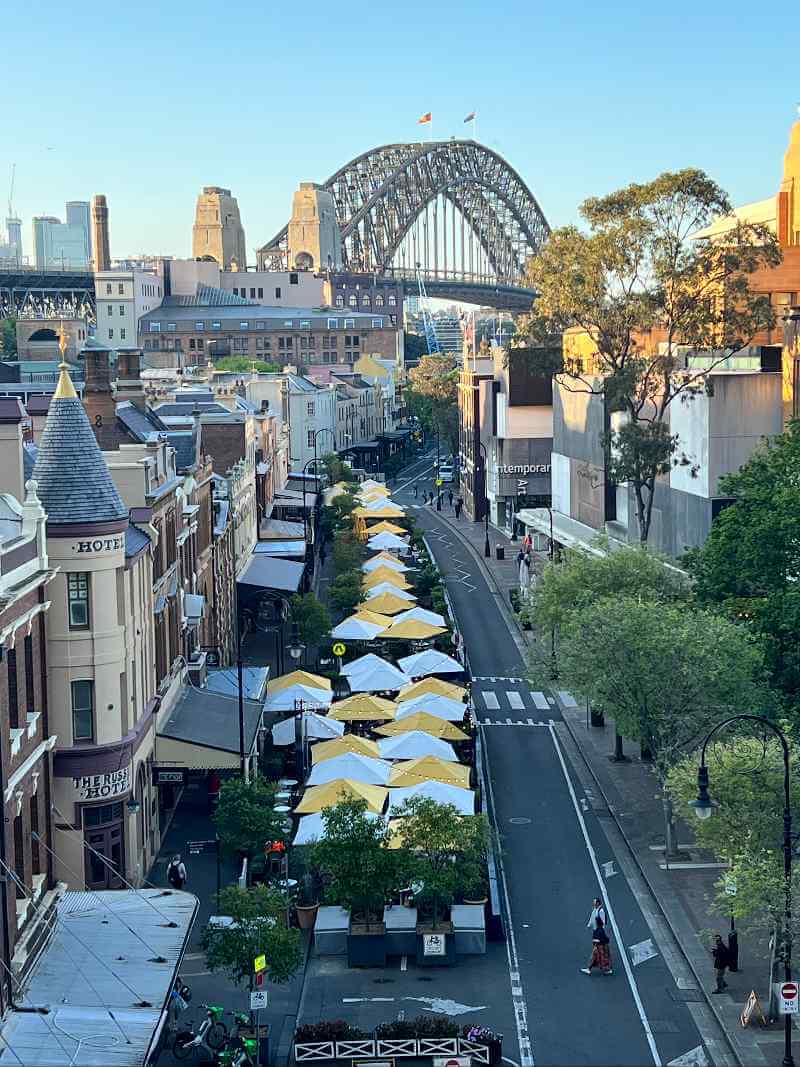 Panorama Sydney ze słynnym mostem Harbour Bridge oraz historyczną dzielnicą The Rocks przy bezchmurnym niebie.